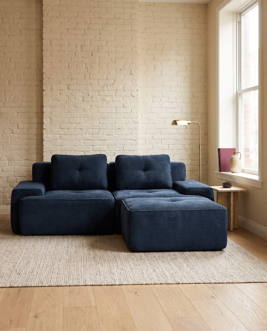 Navy corduroy modular loveseat with a matching ottoman by a window