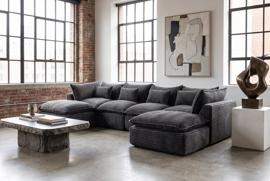 Charcoal corduroy modular sectional with an ottoman in a loft with brick walls and tall windows