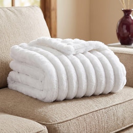 White ribbed faux fur throw, folded on a beige sofa
